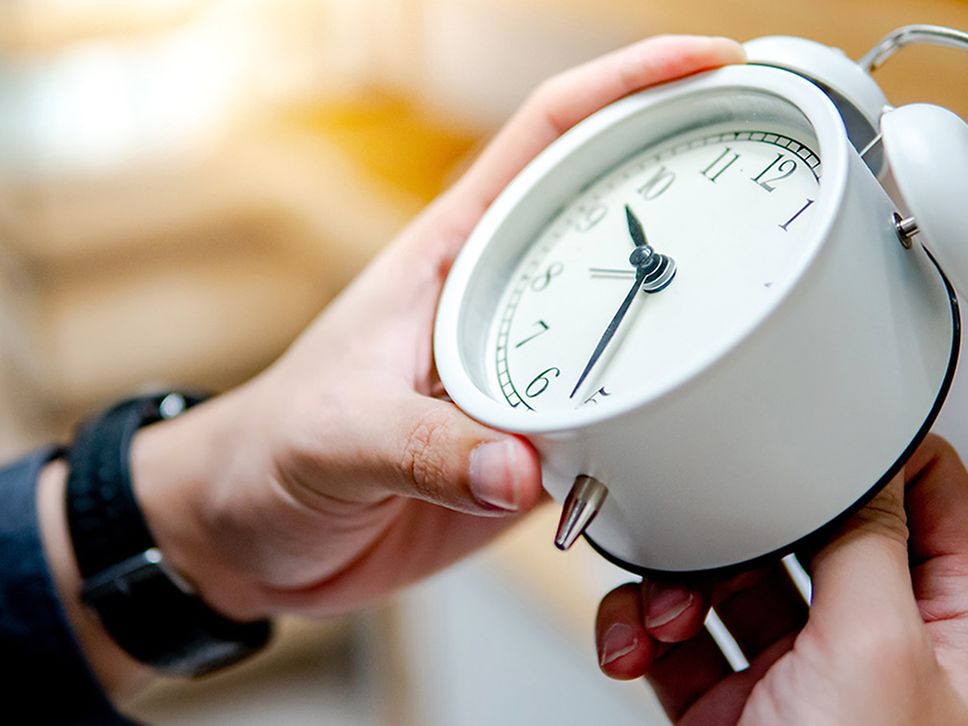 Person hält einen weißen Wecker in der Hand