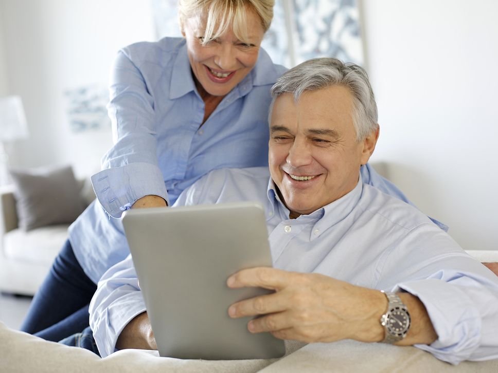 Ein älteres Ehepaar schaut gemeinsam lächelnd auf ein iPad